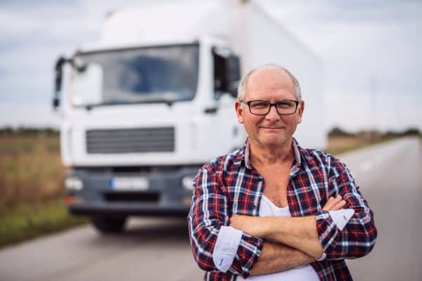 Portrait of a truck driver with crossed arms standing in front of the truck.
