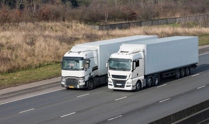 Two white trucks driving side-by-side on the road